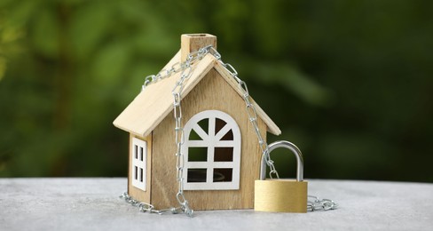 Photo of Home security. House model, chain and padlock on light grey table outdoors, closeup