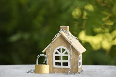 Photo of Home security. House model, chain and padlock on light grey table outdoors, closeup