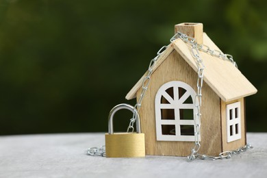 Photo of Home security. House model, chain and padlock on light grey table outdoors, closeup. Space for text