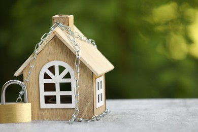 Photo of Home security. House model, chain and padlock on light grey table outdoors, closeup. Space for text