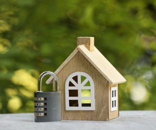 Photo of Home security. House model and padlock on light grey table outdoors, closeup