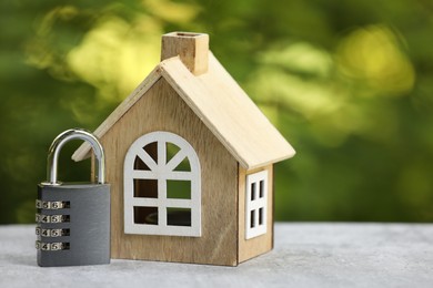 Photo of Home security. House model and padlock on light grey table outdoors, closeup. Space for text