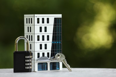 Photo of Home security. House model, key and padlock on light grey table outdoors, closeup. Space for text