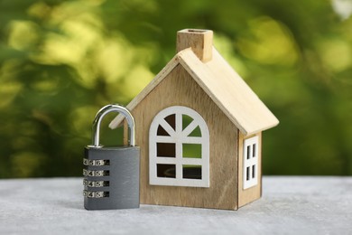 Photo of Home security. House model and padlock on light grey table outdoors, closeup