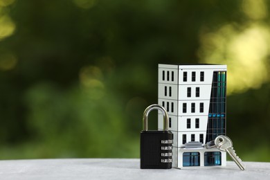 Photo of Home security. House model, key and padlock on light grey table outdoors, closeup. Space for text
