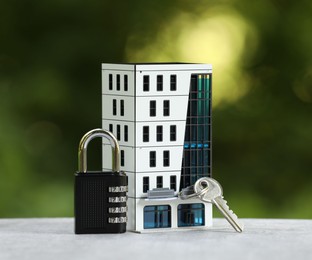 Photo of Home security. House model, key and padlock on light grey table outdoors, closeup