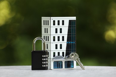 Photo of Home security. House model, key and padlock on light grey table outdoors, closeup