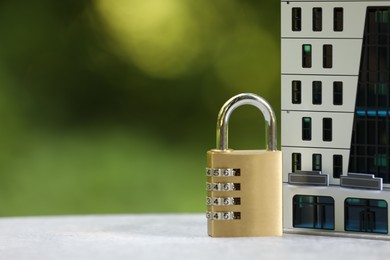 Photo of Home security. House model and padlock on light grey table outdoors, closeup. Space for text