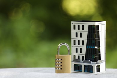 Photo of Home security. House model and padlock on light grey table outdoors, closeup. Space for text