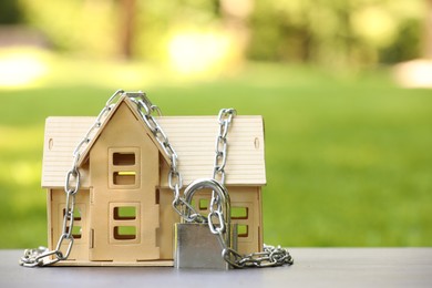 Photo of Home security. House model, chain and padlock on light table outdoors, closeup. Space for text