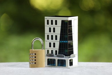 Photo of Home security. House model and padlock on light table outdoors, closeup