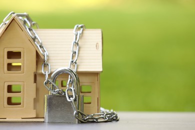 Photo of Home security. House model, chain and padlock on light table outdoors, closeup. Space for text