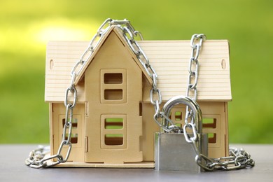 Photo of Home security. House model, chain and padlock on light table outdoors, closeup