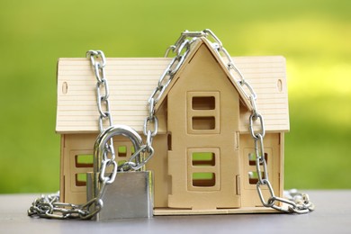 Photo of Home security. House model, chain and padlock on light table outdoors, closeup