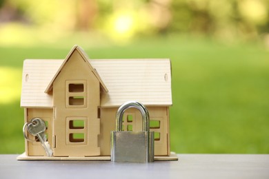 Photo of Home security. House model, key and padlock on light table outdoors, closeup. Space for text