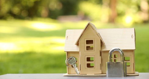 Photo of Home security. House model, key and padlock on light table outdoors, closeup. Space for text