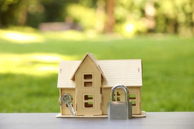 Photo of Home security. House model, key and padlock on light table outdoors, closeup