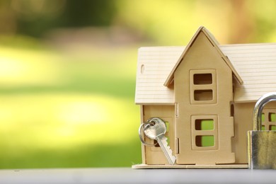 Photo of Home security. House model, key and padlock on light table outdoors, closeup. Space for text