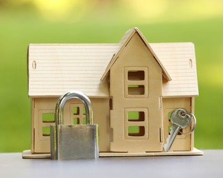 Photo of Home security. House model, key and padlock on light table outdoors, closeup