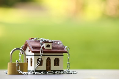 Photo of Home security. House model, chain and padlock on light table outdoors, closeup. Space for text