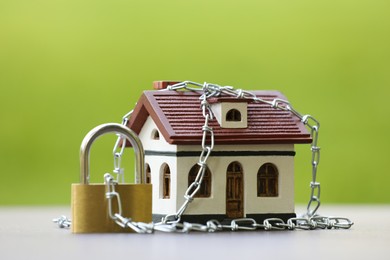 Photo of Home security. House model, chain and padlock on light table outdoors, closeup