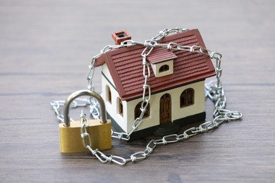 Photo of Home security. House model, chain and padlock on wooden table outdoors, closeup