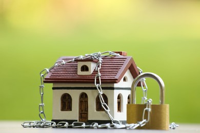 Photo of Home security. House model, chain and padlock on white table outdoors, closeup