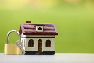 Photo of Home security. House model, key and padlock on white table outdoors, closeup. Space for text