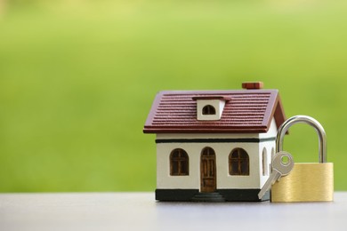 Photo of Home security. House model, key and padlock on white table outdoors, closeup. Space for text