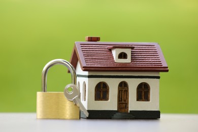 Photo of Home security. House model, key and padlock on white table outdoors, closeup