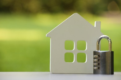 Photo of Home security. House model and padlock on white table outdoors, closeup. Space for text