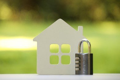 Photo of Home security. House model and padlock on white table outdoors, closeup