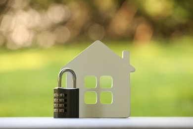 Photo of Home security. House model and padlock on white table outdoors, closeup