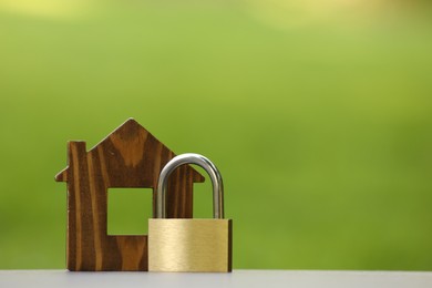 Photo of Home security. House model and padlock on light grey table outdoors, closeup. Space for text