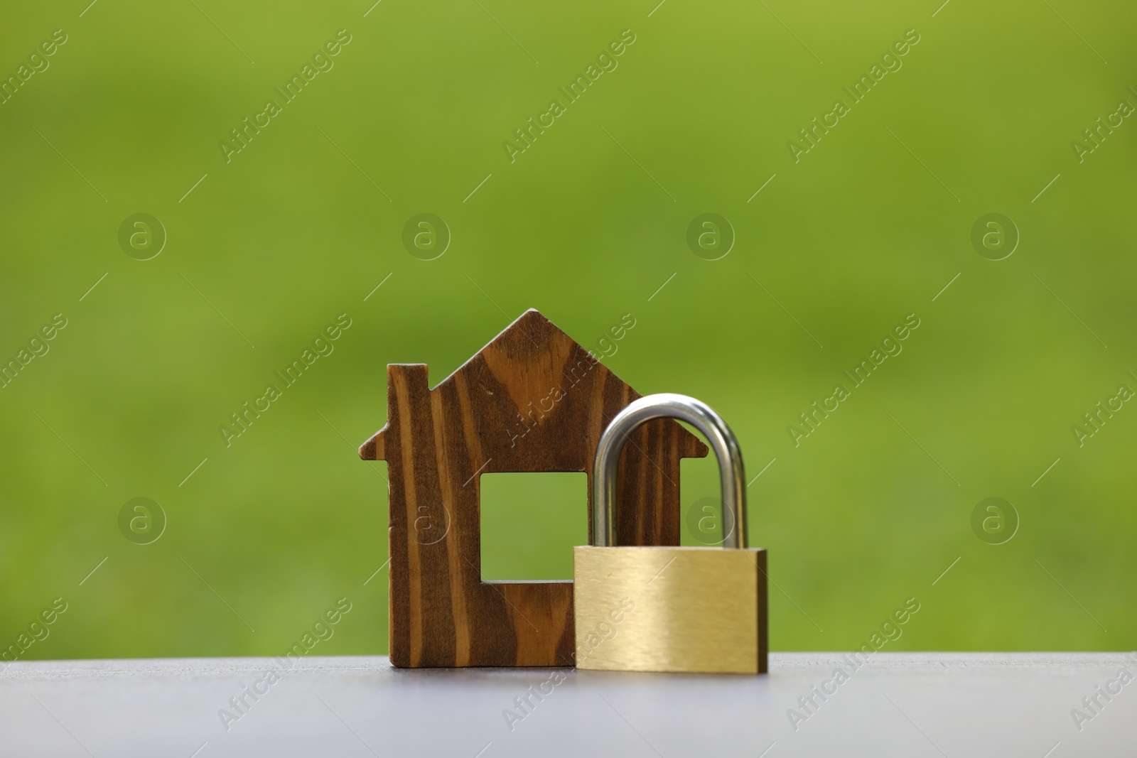 Photo of Home security. House model and padlock on light grey table outdoors, closeup