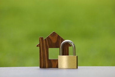 Photo of Home security. House model and padlock on light grey table outdoors, closeup