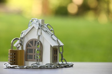 Photo of Home security. House model, chain and padlock on light grey table outdoors, closeup. Space for text