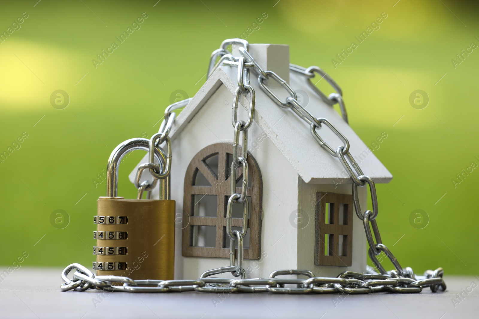 Photo of Home security. House model, chain and padlock on light grey table outdoors, closeup