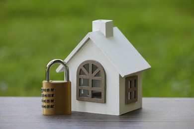 Photo of Home security. House model and padlock on wooden table outdoors, closeup