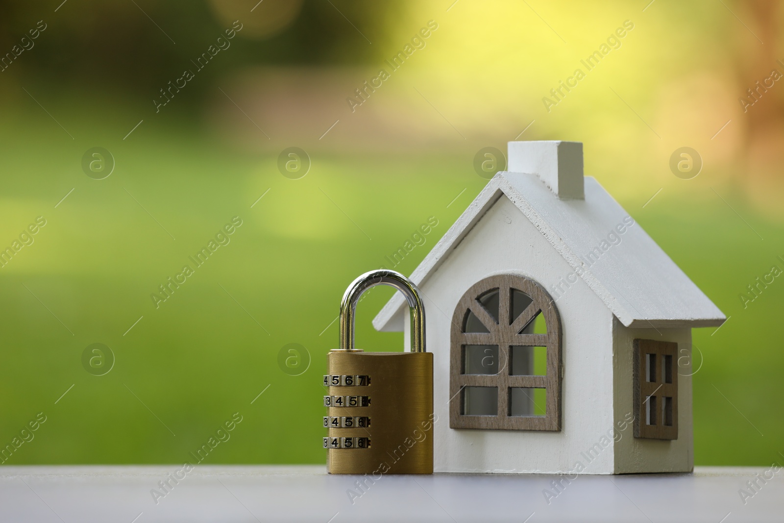 Photo of Home security. House model and padlock on light grey table outdoors, closeup. Space for text