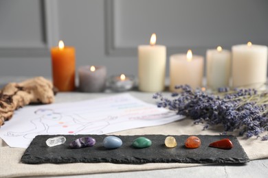 Photo of Chakra gemstones, lavender flowers, human drawing and burning candles on light table, selective focus
