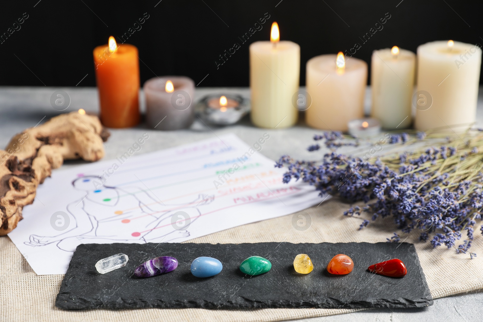 Chakra gemstones, lavender flowers, human drawing and burning candles on light table, selective focus Photo of Chakra gemstones, lavender flowers, human drawing and burning candles on light table, selective focus