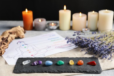 Photo of Chakra gemstones, lavender flowers, human drawing and burning candles on light table, selective focus