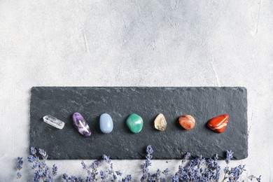 Photo of Chakra gemstones and lavender flowers on light table, flat lay. Space for text