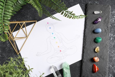 Photo of Drawing of chakras on human body, gemstones, and plants on black table, flat lay