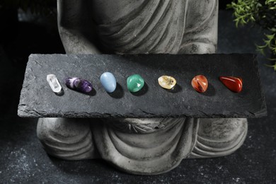 Photo of Statue with chakra gemstones on black table, closeup