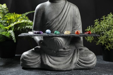 Photo of Statue with chakra gemstones and plants on black table, closeup