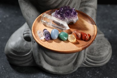 Photo of Statue with chakra gemstones on black table, closeup
