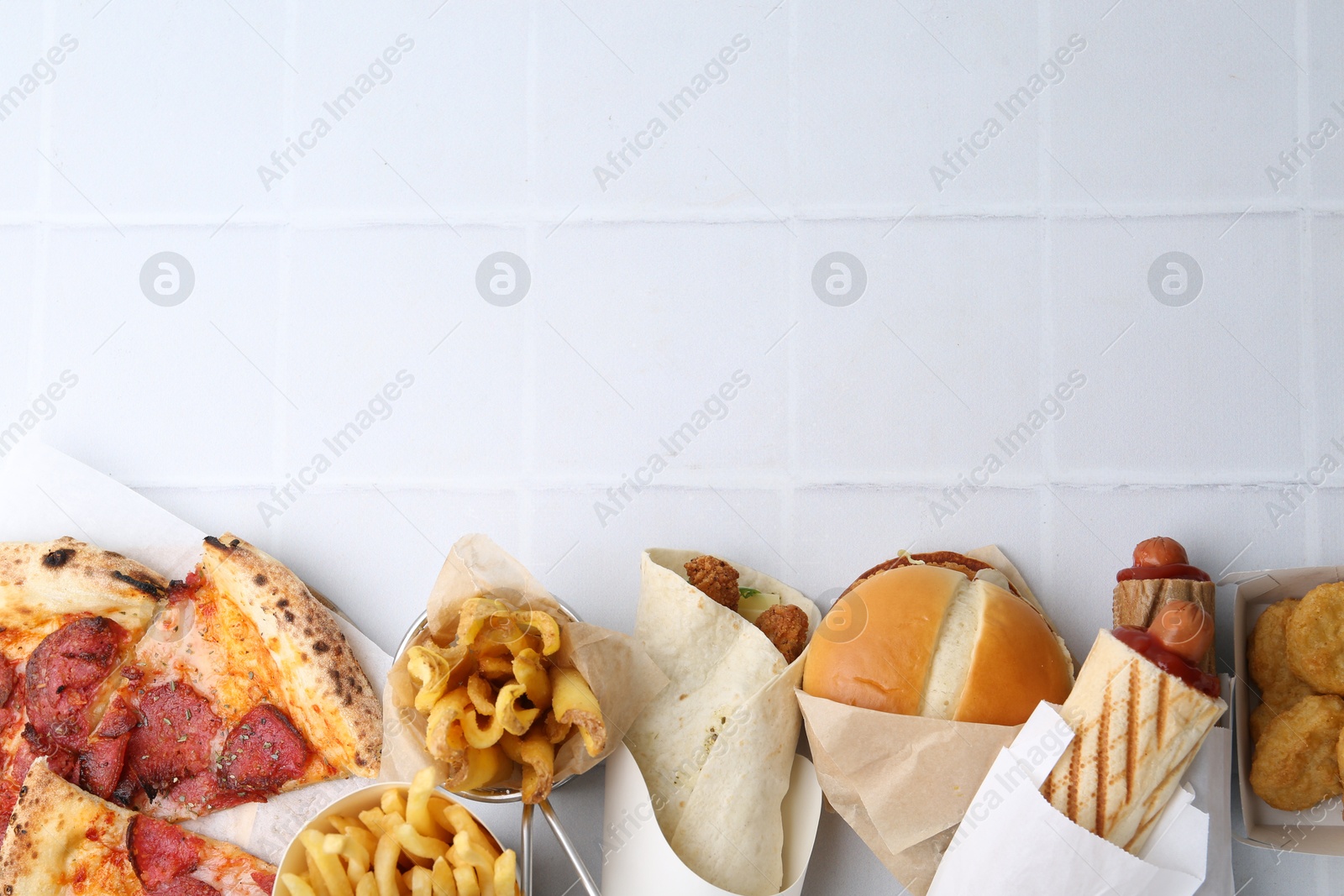 Different delicious fast food on white tiled table, flat lay. Space for text Photo of Different delicious fast food on white tiled table, flat lay. Space for text