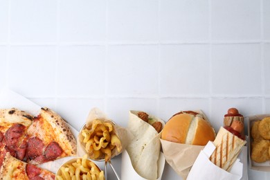 Photo of Different delicious fast food on white tiled table, flat lay. Space for text